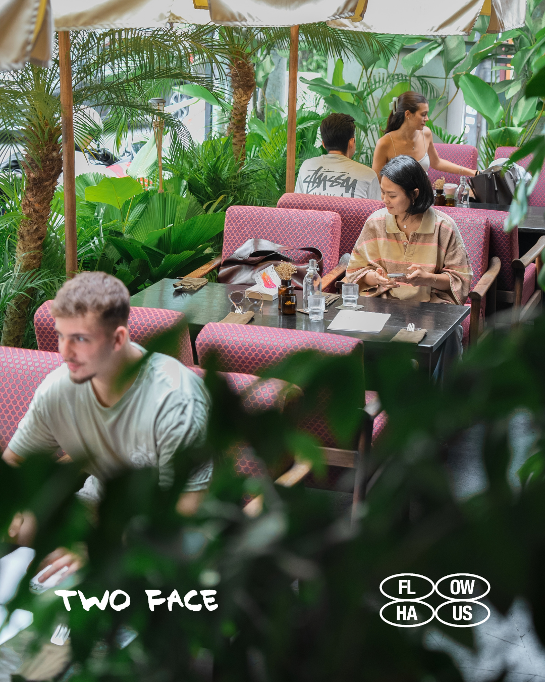 Guests at pink tables on TWO FACE's leafy terrace, with the TWO FACE and FLOW HAUS PROJECT logos