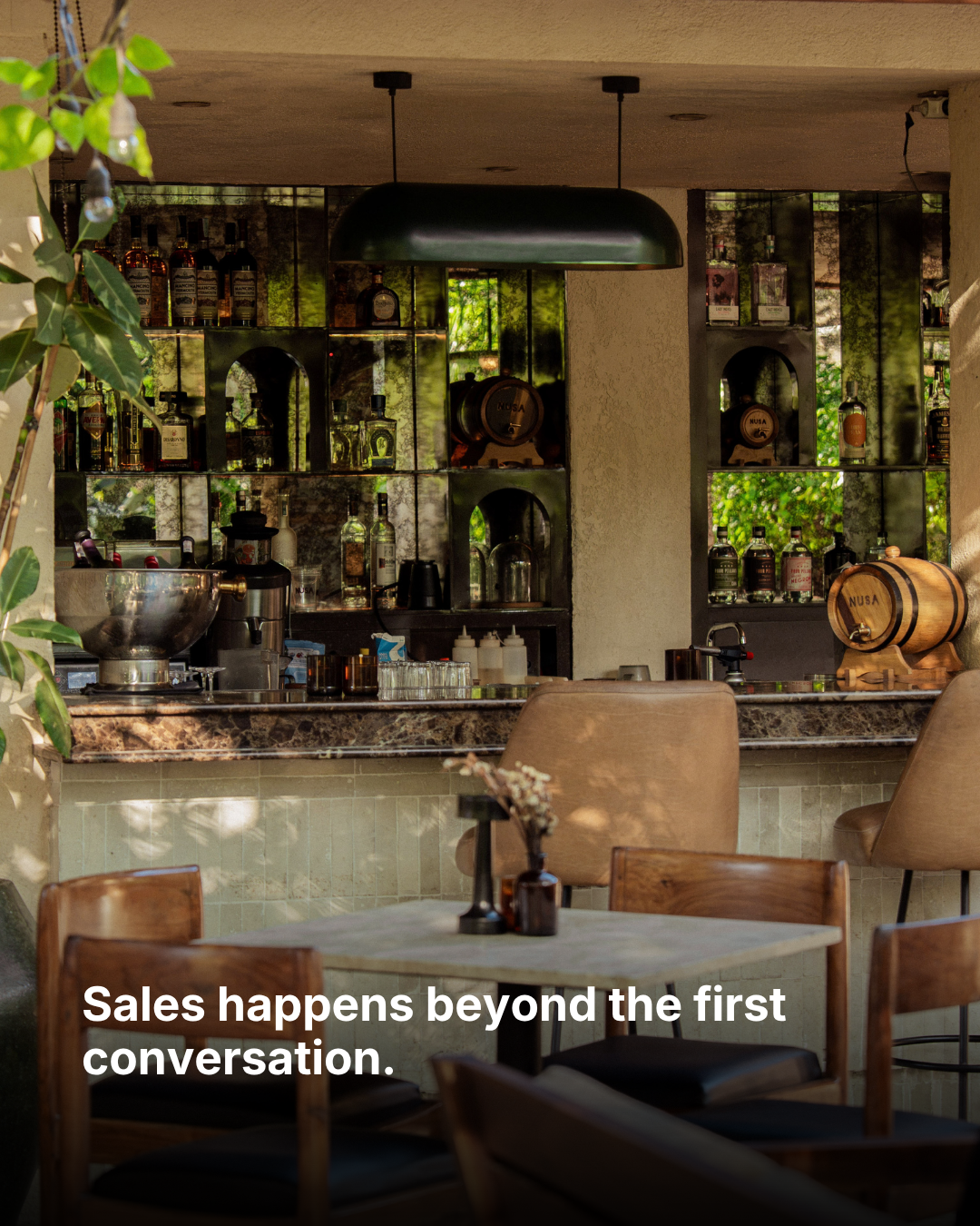 A dining room with greenery and a bar, with the words “Sales happens beyond the first conversation.”