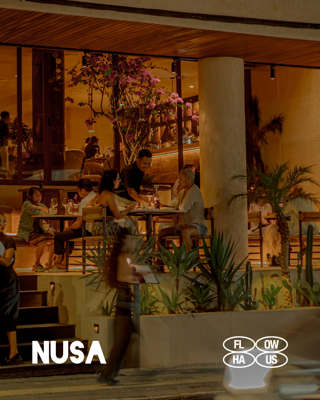 The open, plant-filled dining room at NUSA, with the NUSA and FLOW HAUS PROJECT logos